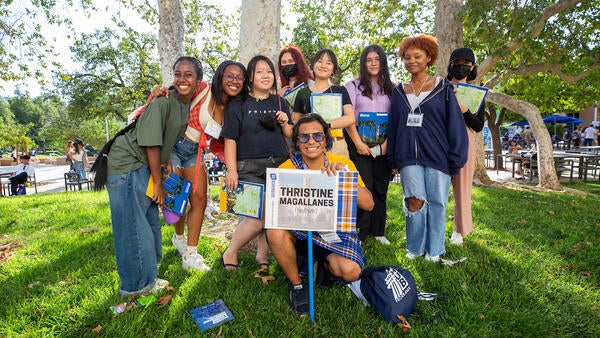 A group of students stand on the grass outside around an orientation leader carrying a leader sign.