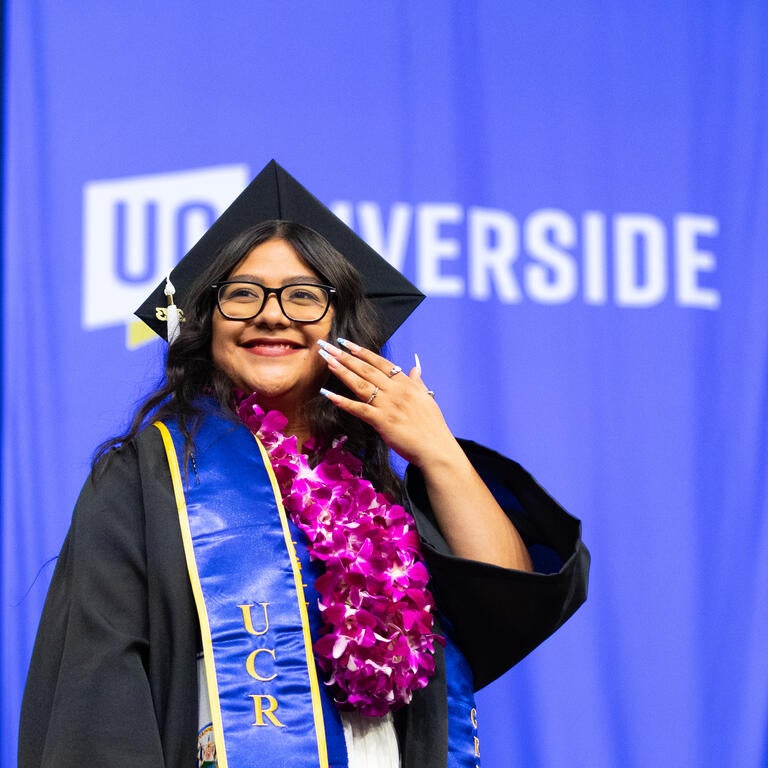 A student stands in front of the campus UCR letters holding a UC Riverside pennant flag