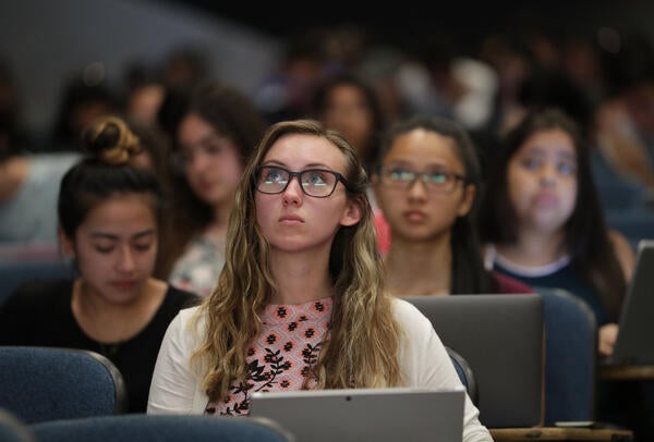 A student sits in a lecture room surrounded by other students