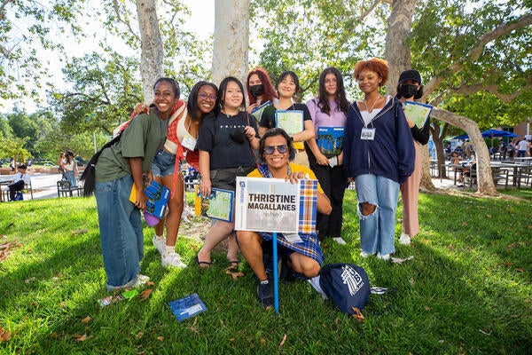 A group of students stand on the grass outside around an orientation leader carrying a leader sign.