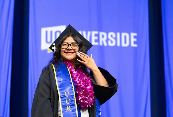 A student stands in front of the campus UCR letters holding a UC Riverside pennant flag