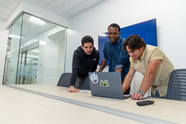 Three students gather around a computer screen