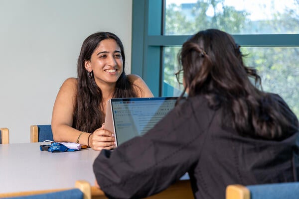 Two students talk to each other at a table