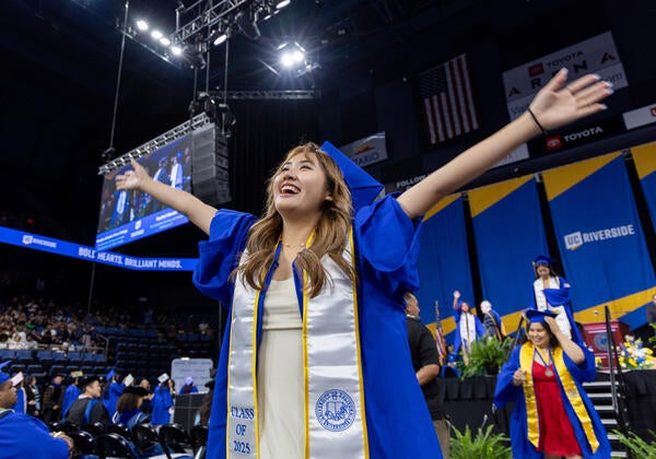 A graduate walks off of the graduation stage with her arms spread