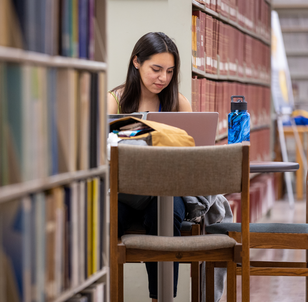 A student sits in the UCR library at a desk with a laptop